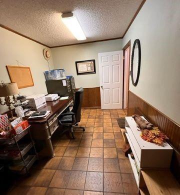 home office featuring wood walls, crown molding, a textured ceiling, and wainscoting