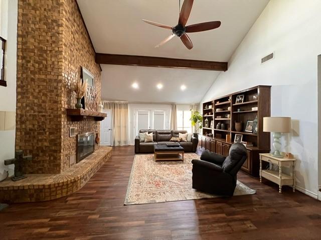 living room featuring beam ceiling, dark wood finished floors, a fireplace, visible vents, and high vaulted ceiling