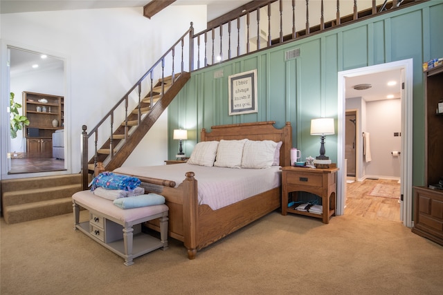 bedroom featuring a towering ceiling, beam ceiling, and light colored carpet