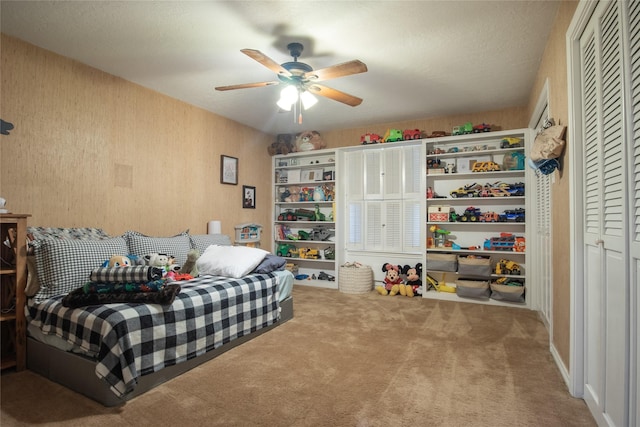 carpeted bedroom with a ceiling fan, a closet, a textured ceiling, and wallpapered walls