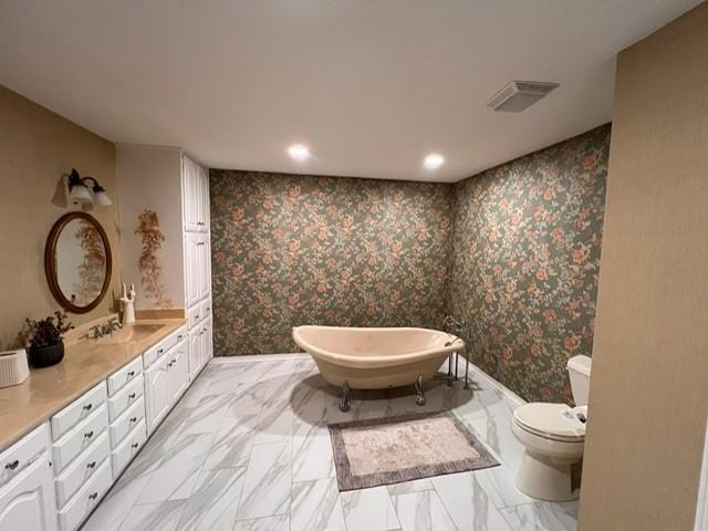 full bathroom with toilet, wallpapered walls, a freestanding bath, and vanity