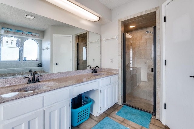 full bath with double vanity, a stall shower, a textured ceiling, and a sink