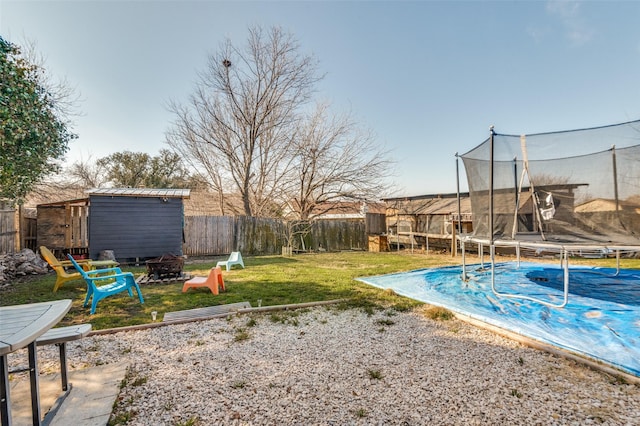 view of yard with a fire pit, a fenced backyard, an outbuilding, a trampoline, and a storage unit