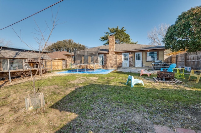 rear view of house with an outdoor fire pit, a lawn, a chimney, a trampoline, and fence