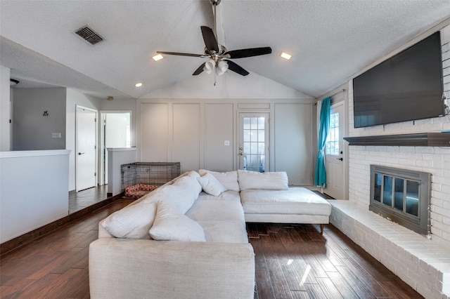 living area with a textured ceiling, a decorative wall, a fireplace, wood finished floors, and visible vents