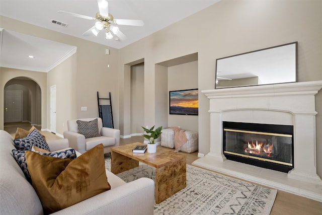 living room with arched walkways, a ceiling fan, a glass covered fireplace, wood finished floors, and baseboards