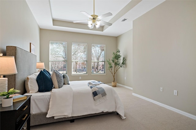 bedroom with light colored carpet, visible vents, baseboards, a ceiling fan, and a tray ceiling