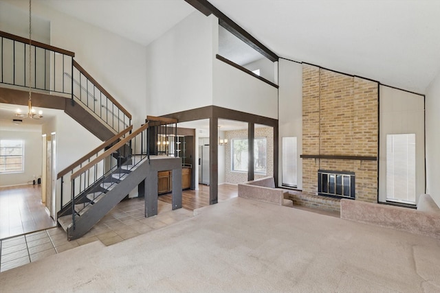 unfurnished living room featuring a chandelier, high vaulted ceiling, carpet floors, a fireplace, and stairs