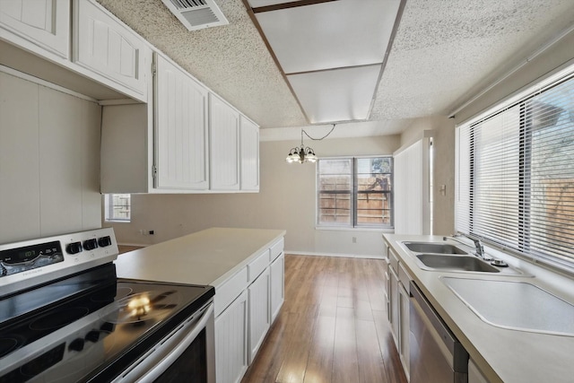 kitchen with light wood-style flooring, a sink, white cabinets, light countertops, and appliances with stainless steel finishes