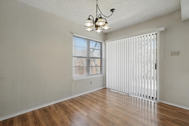 spare room with a chandelier, a textured ceiling, baseboards, and wood finished floors