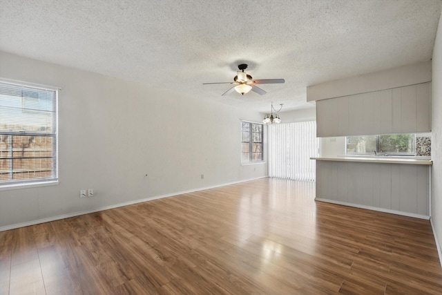 unfurnished living room featuring ceiling fan with notable chandelier, a textured ceiling, baseboards, and wood finished floors