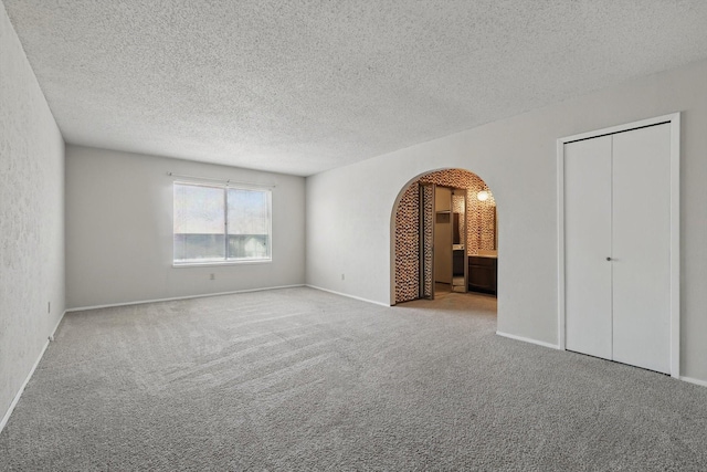 unfurnished bedroom with carpet floors, arched walkways, and a textured ceiling