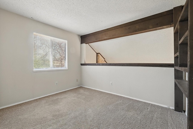 empty room with carpet floors, beam ceiling, a textured ceiling, and baseboards