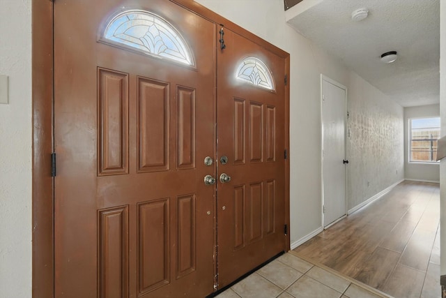 foyer with a textured ceiling, baseboards, and light tile patterned floors