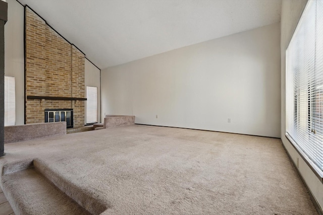 unfurnished living room featuring high vaulted ceiling, a brick fireplace, and light colored carpet