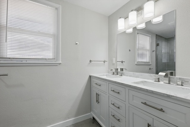 bathroom featuring double vanity, a sink, baseboards, and a tile shower