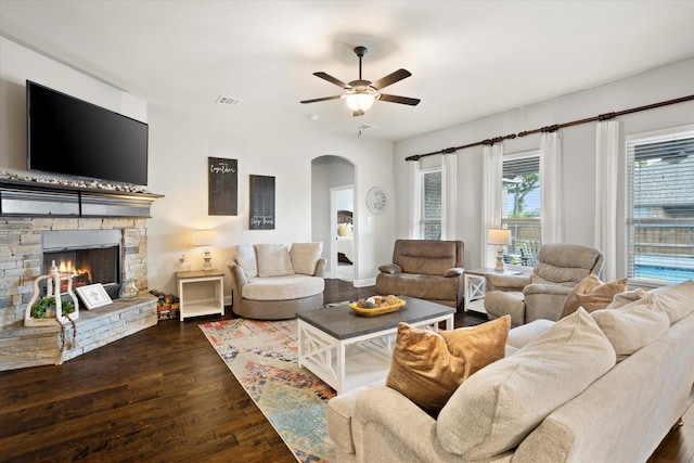 living room with visible vents, arched walkways, ceiling fan, wood-type flooring, and a stone fireplace