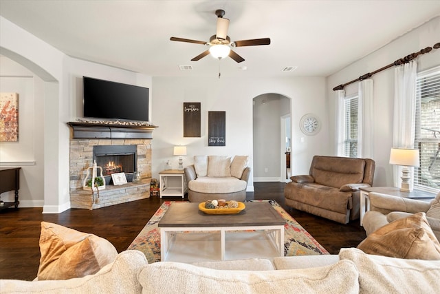 living room with arched walkways, a fireplace, wood finished floors, visible vents, and baseboards