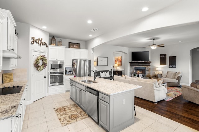 kitchen featuring arched walkways, appliances with stainless steel finishes, under cabinet range hood, a fireplace, and a sink