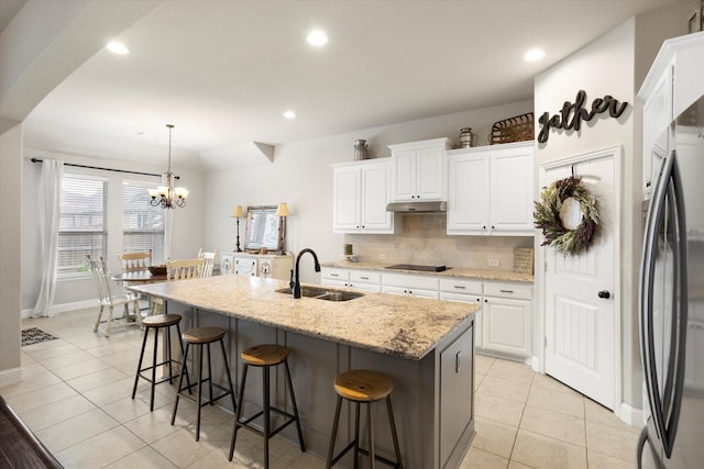 kitchen with a kitchen breakfast bar, a sink, under cabinet range hood, black appliances, and backsplash