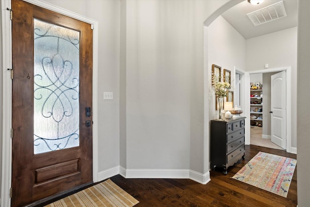 foyer with arched walkways, dark wood-style flooring, visible vents, and baseboards