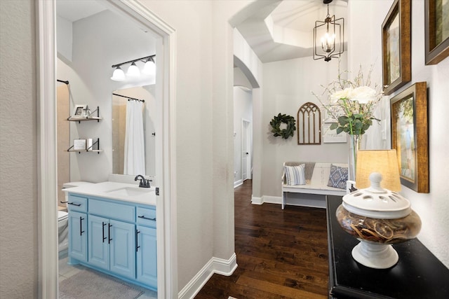 hall featuring baseboards, arched walkways, wood finished floors, a chandelier, and a sink