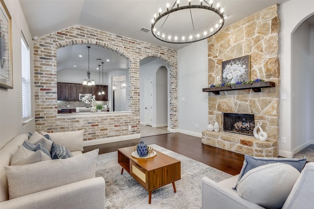 living area featuring visible vents, arched walkways, wood finished floors, vaulted ceiling, and a stone fireplace