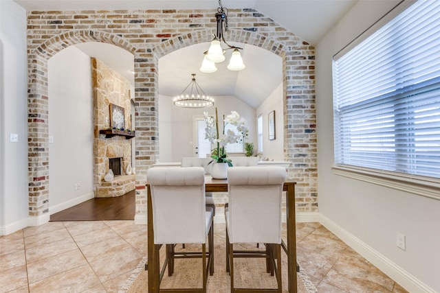 tiled dining space featuring a fireplace, baseboards, vaulted ceiling, and a notable chandelier