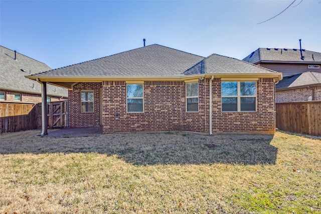 rear view of house featuring a yard, a fenced backyard, a shingled roof, and brick siding