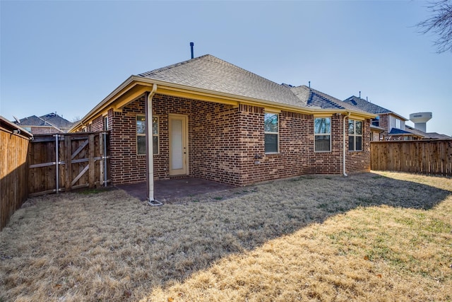 rear view of property featuring a yard, brick siding, a fenced backyard, and a gate