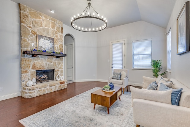 living room featuring lofted ceiling, arched walkways, a stone fireplace, a notable chandelier, and wood finished floors