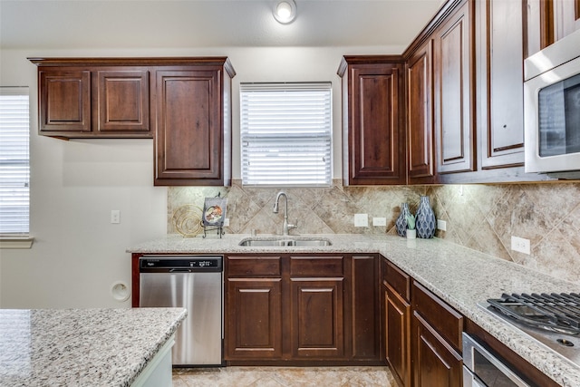 kitchen featuring a sink, dark brown cabinets, appliances with stainless steel finishes, backsplash, and light stone countertops