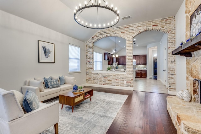 living room featuring arched walkways, lofted ceiling, brick wall, dark wood-style flooring, and visible vents