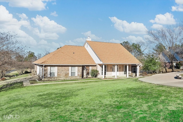 view of front facade featuring a chimney, roof with shingles, a front lawn, a porch, and brick siding