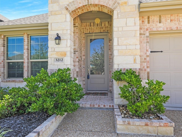 property entrance with stone siding, a shingled roof, an attached garage, and brick siding