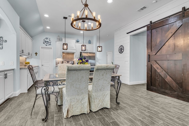 dining space with a barn door, wood finished floors, visible vents, and recessed lighting