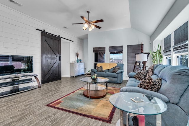 living room featuring a barn door, visible vents, lofted ceiling, ceiling fan, and wood finished floors