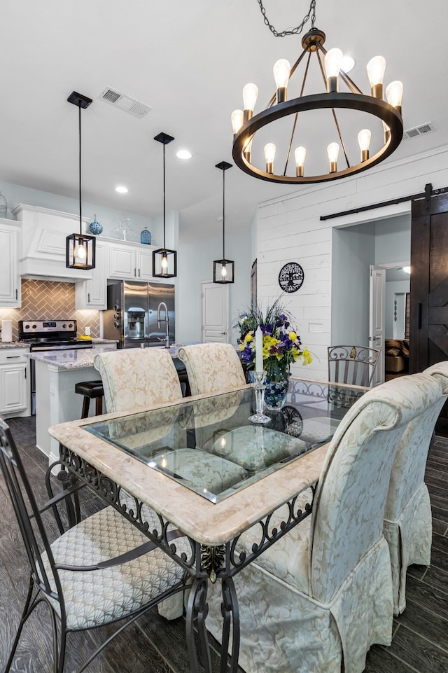 dining area featuring a barn door, dark wood finished floors, visible vents, and an inviting chandelier