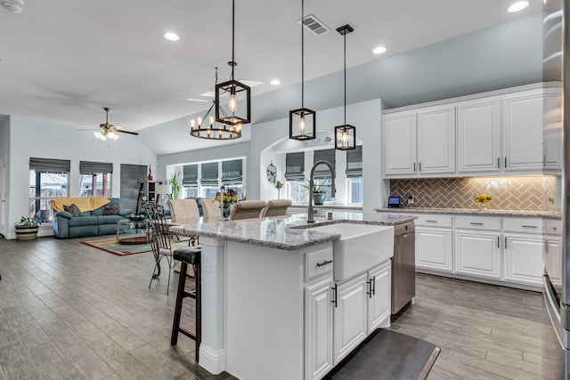 kitchen with light wood finished floors, an island with sink, vaulted ceiling, stainless steel dishwasher, and a sink