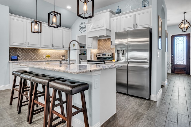 kitchen with lofted ceiling, appliances with stainless steel finishes, wood tiled floor, white cabinets, and premium range hood