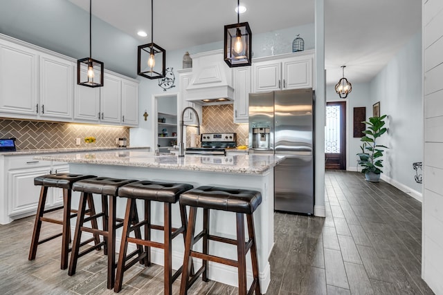 kitchen with light stone counters, a sink, wood finished floors, white cabinets, and stainless steel fridge