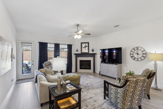 living room with a glass covered fireplace, visible vents, baseboards, and wood finished floors