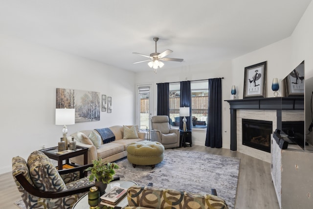 living area with a ceiling fan, wood finished floors, and a glass covered fireplace