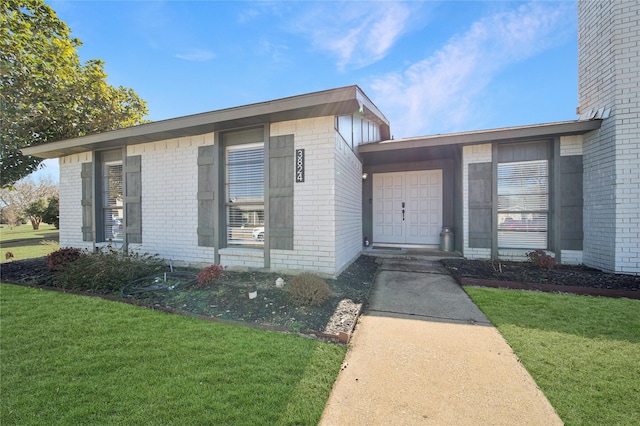 entrance to property with brick siding and a lawn