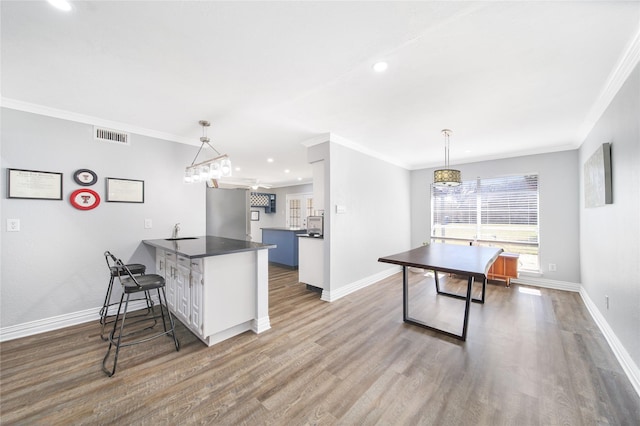 kitchen featuring a sink, a peninsula, wood finished floors, and crown molding