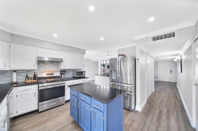 kitchen with visible vents, dark countertops, wall chimney exhaust hood, appliances with stainless steel finishes, and blue cabinets