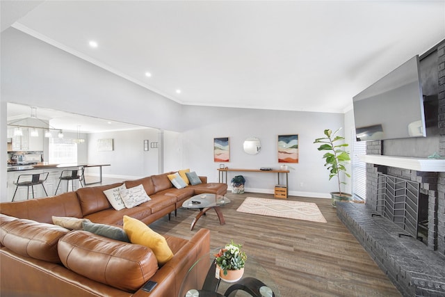 living room with baseboards, wood finished floors, vaulted ceiling, crown molding, and a fireplace