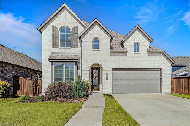 french country home with brick siding, a front yard, fence, a garage, and driveway