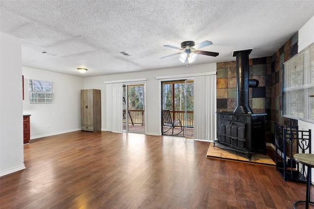 unfurnished living room featuring visible vents, a wood stove, a textured ceiling, wood finished floors, and baseboards