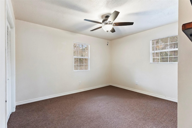 empty room featuring ceiling fan, dark carpet, baseboards, and a textured ceiling